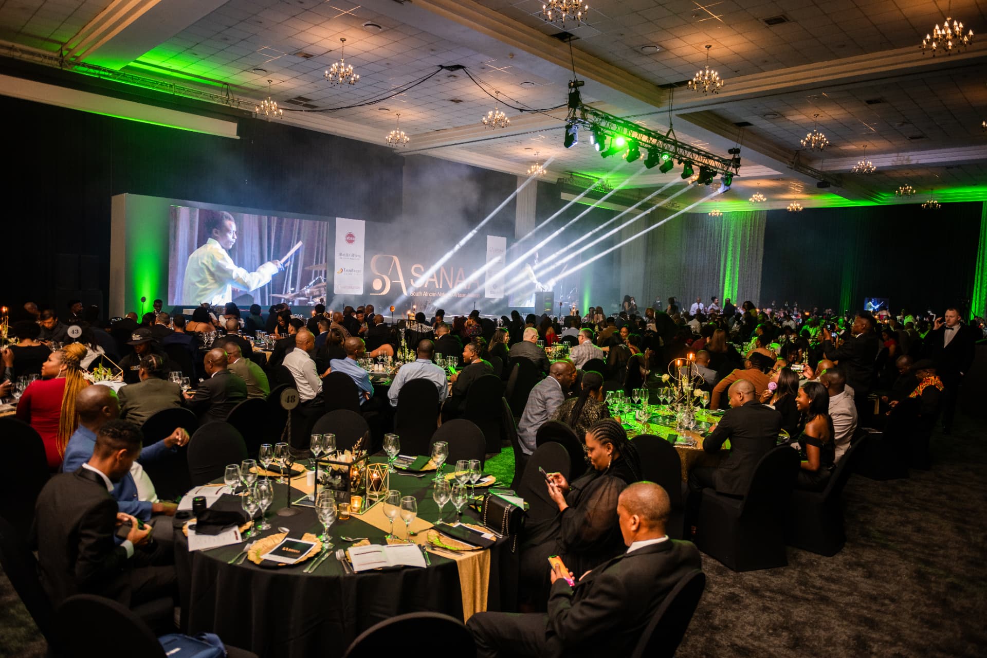 Wide view of guests gathered in the SANAA gala ballroom under green stage lighting